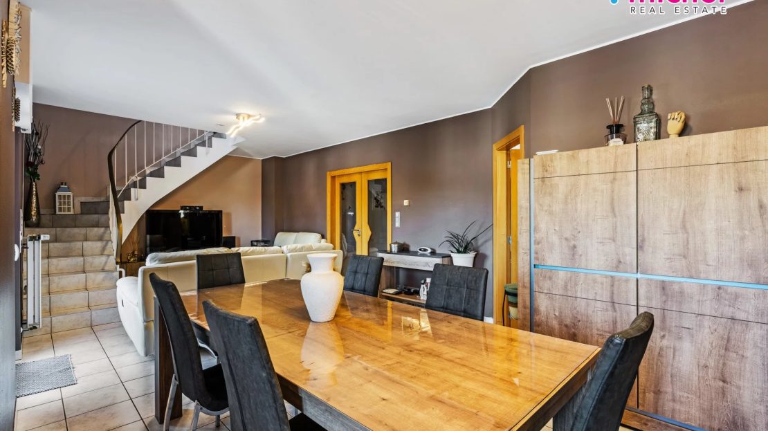 Dining room with a large wooden table and chairs, tall storage cabinets, television seating, and an internal staircase.
