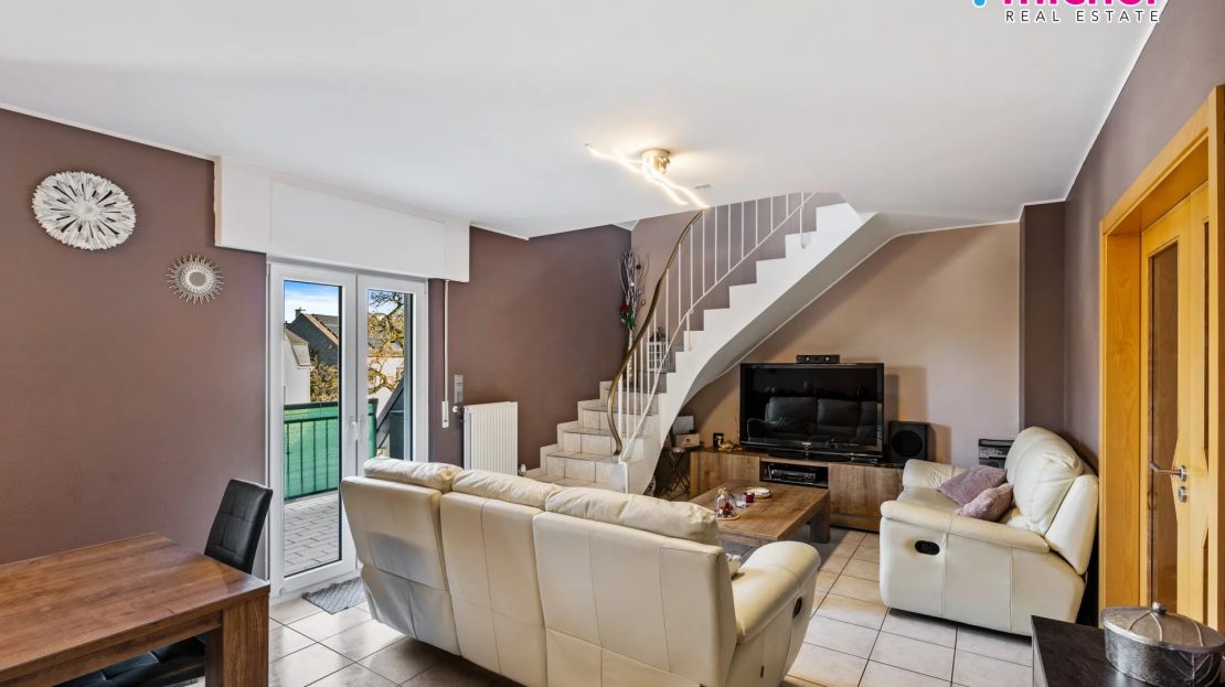 Duplex living room with cream seating, television, dining table, internal stairs, and glazed doors leading to a balcony.
