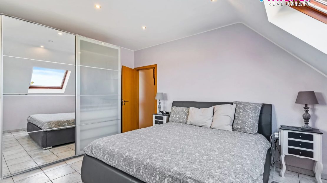 Bedroom with a large bed, mirrored sliding wardrobe, bedside tables, and a skylight in the sloping ceiling.